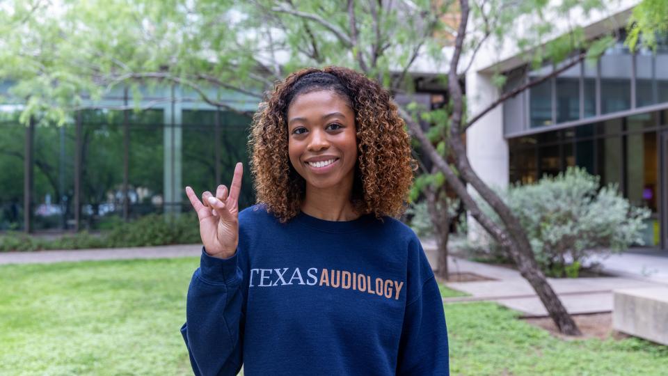 Woman in a Texas Audiology shirt making the Hook ’em Horns gesture