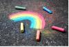 A rainbow drawn on black asphalt with pieces of chalk around it.