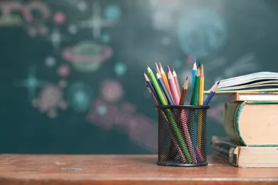 A black mesh cup filled with colored pencils and a stack of books beside it.