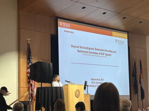 Sajana Aryal standing at a podium in front of a powerpoint presentation