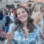 White woman. Head tilted to the left. She is smiling with blue eyes. Hair is brown, curled, and just past shoulder length. Wearing and blue and white floral long-sleeve top. UT horns up.