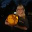 Blonde Allison Choi holding a carved pumpkin outside at night