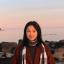 Xinming standing on the shore at sunset in a red jacket and striped scarf